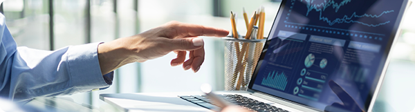 Image of hand pointing at a laptop screen with graphs and charts on it.